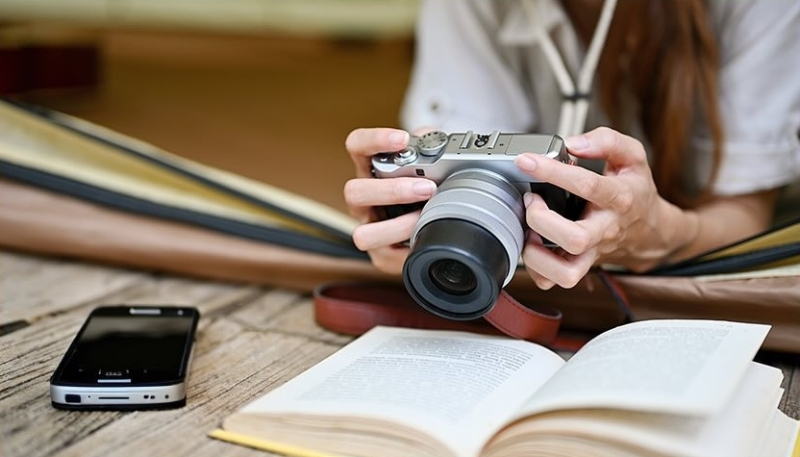 cámara de fotos sostenida por una mujer sobre un escritorio con un libro de texto y un móvil